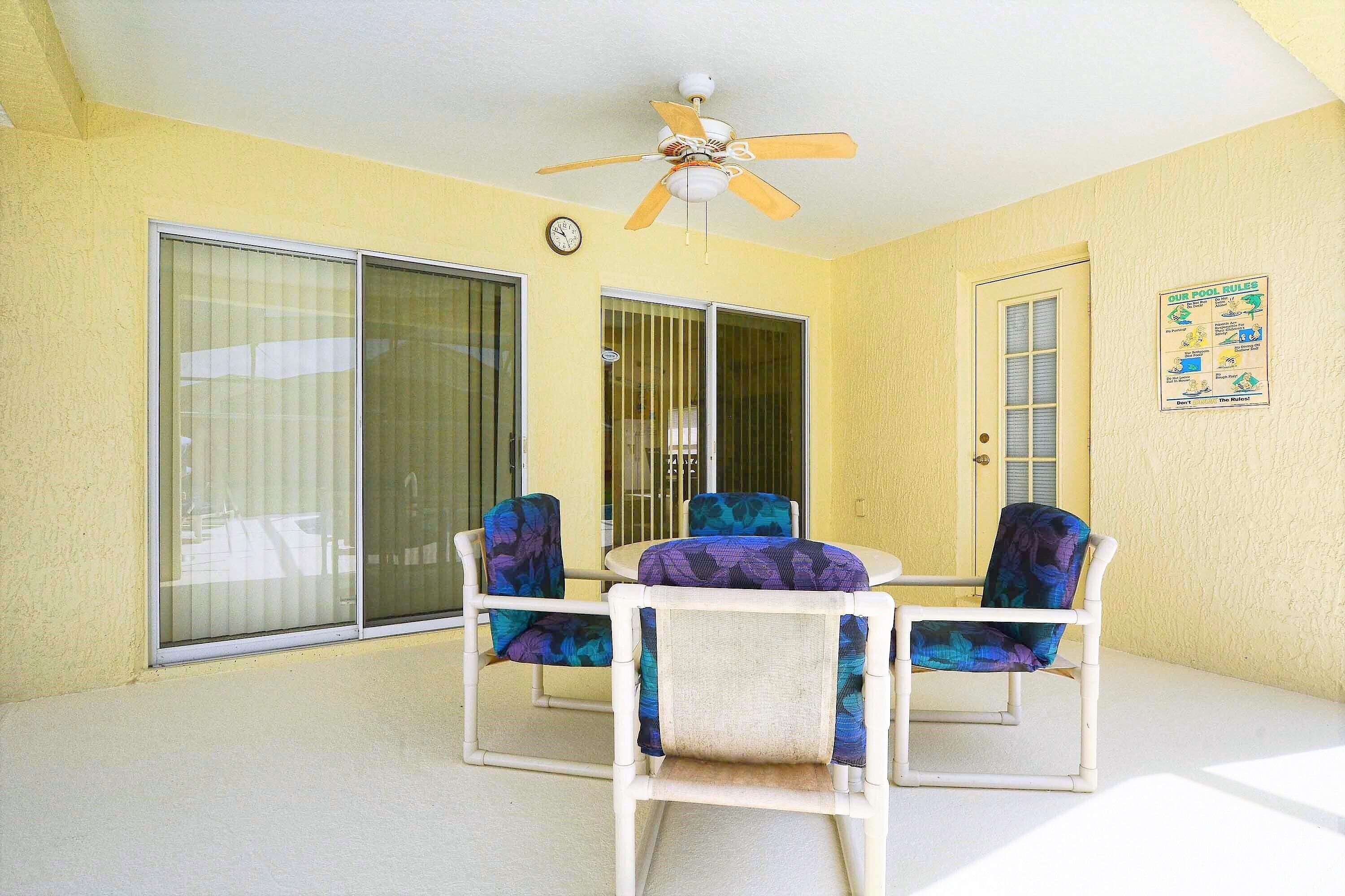 Una habitación con ventilador de techo, una mesa con sillas, una ventana con persianas y una puerta.