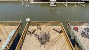 A wooden deck with a round table and chairs, surrounded by a railing. - Spacious Waterfront Retreat | Balcony, Huge Deck & Views (Corpus Christi)
