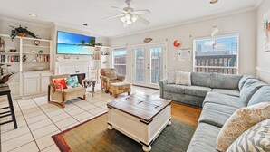 Un salon spacieux avec un canapé gris, une table basse en bois et un téléviseur diffusant une scène de plage.