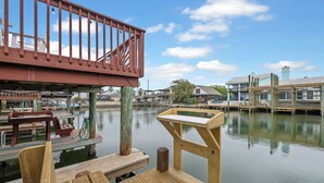 Une terrasse en bois avec une rambarde rouge, donnant sur une étendue d’eau calme, agrémentée de bancs en bois et offrant une vue sur les bâtiments situés de l’autre côté.