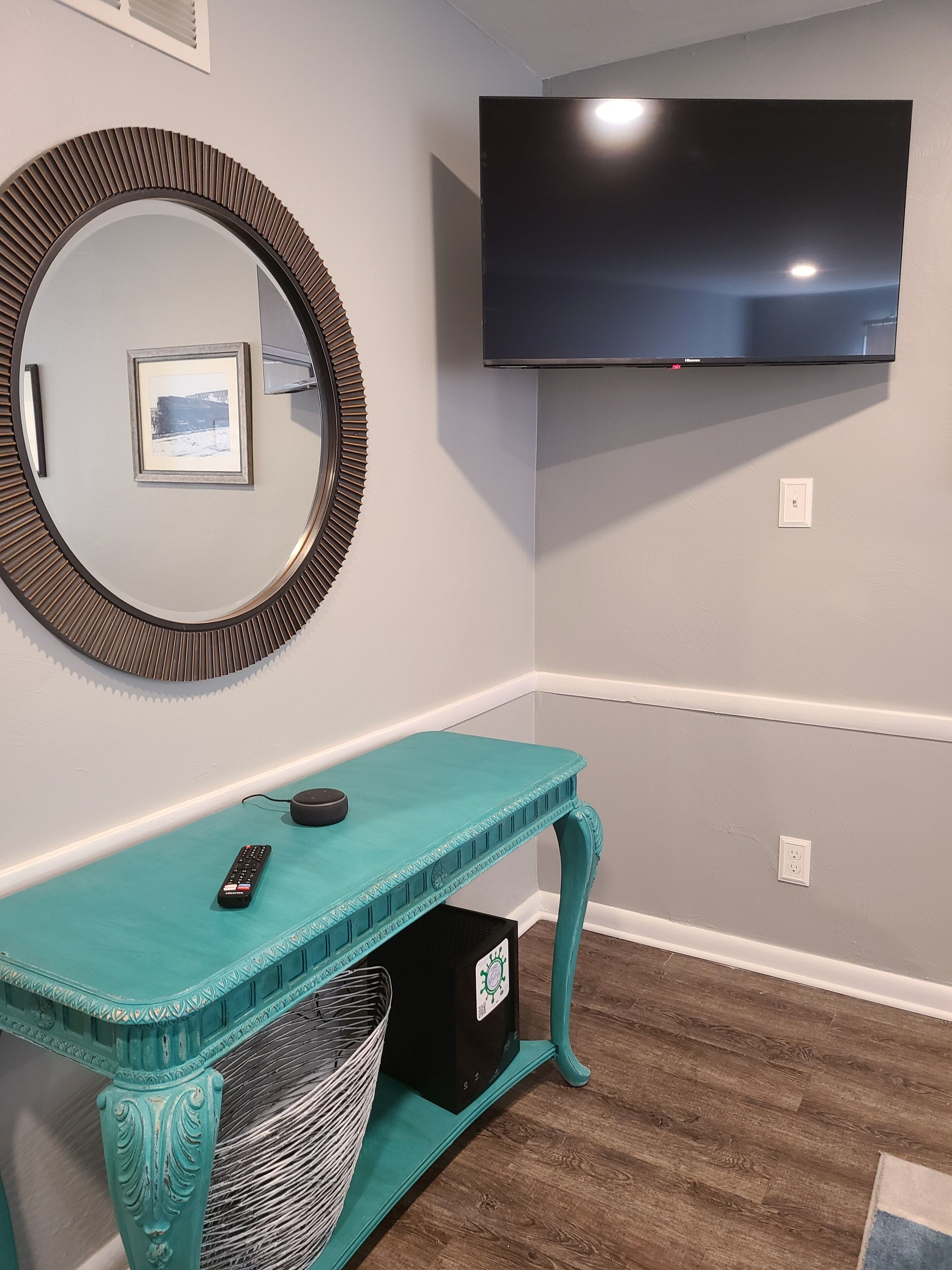A teal console table with a TV mounted above it, a framed picture on the wall, and a power outlet.