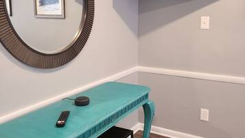 A teal console table with a TV mounted above it, a framed picture on the wall, and a power outlet.