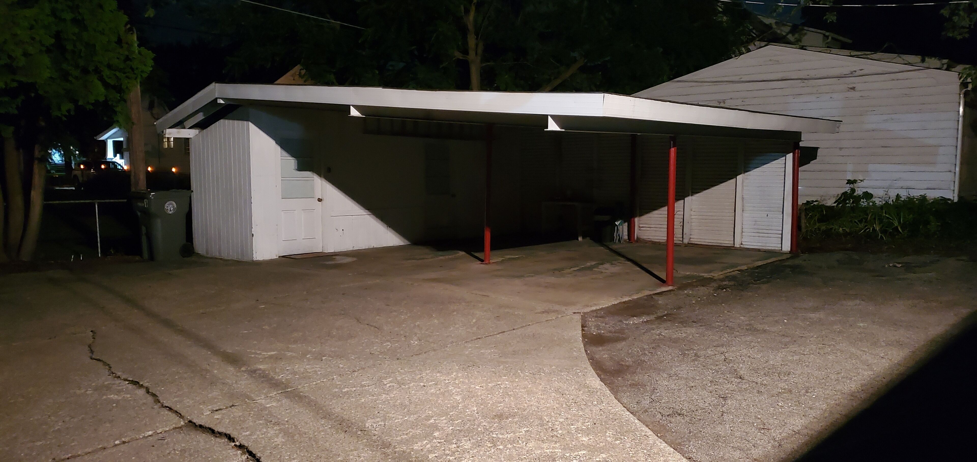 Un garage con un'area di sosta coperta, una porta bianca e una trave di sostegno rossa.