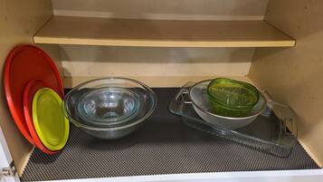 A kitchen with a black mat, a glass bowl, a green strainer, and red and yellow lids.