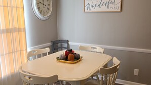 A dining area with a white table and chairs, a clock on the wall, and a sign that says "TOGETHER is a wonderful place to be."