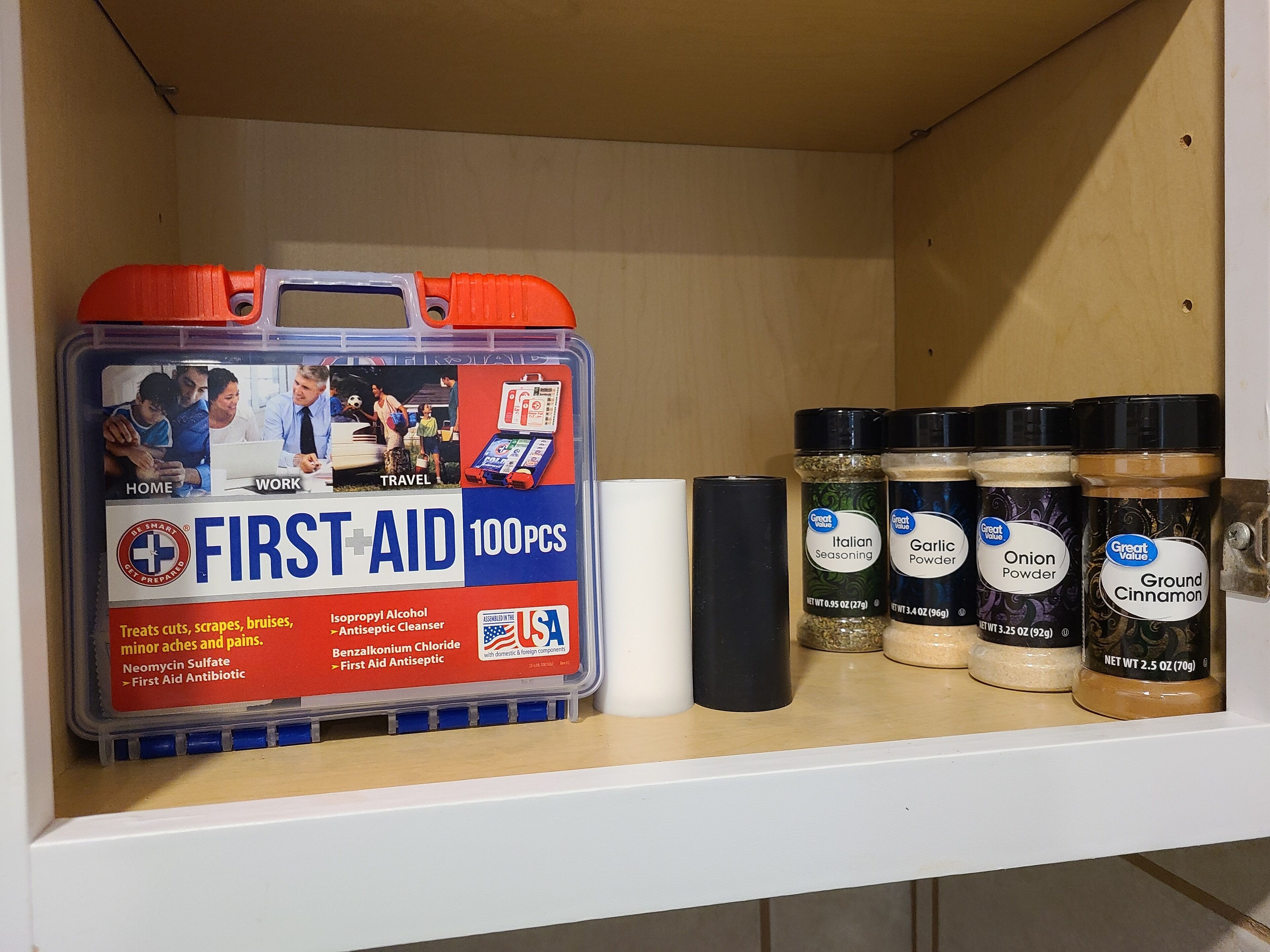 A shelf with a first aid kit and various seasoning jars.