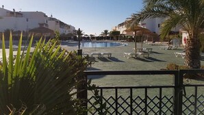 Zona de piscina con sillones de descanso y palmeras, rodeada de edificios.