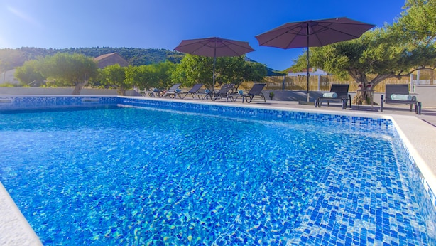 A swimming pool with clear blue water, surrounded by lounge chairs and umbrellas. - Villa Antonia is near Trogir with a private pool (Marina)