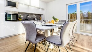 A modern kitchen with white cabinets, a built-in oven, and a dining area with a white table and grey chairs. - Villa Antonia is near Trogir with a private pool (Marina)