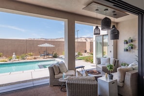 A poolside area with wicker furniture, a fire pit, and hanging pendant lights.