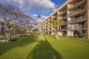 A hotel with multiple balconies, a well-maintained lawn, and a large tree providing shade.