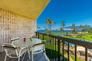 A balcony with a table and chairs, overlooking a golf course and a pool.