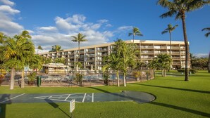 A multi-story hotel with a pool area, surrounded by palm trees and a well-maintained lawn.