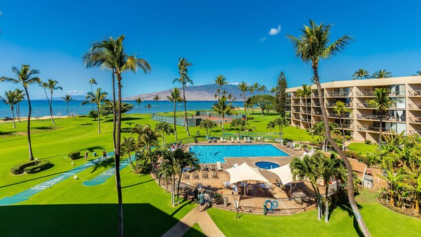 A resort with a pool, palm trees, and a view of the ocean.