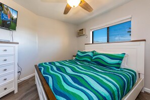 A bedroom with a bed, a dresser, a ceiling fan, and a window with a view of the sky.
