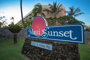 A sign for 'Maui Sunset' with a stone base and a street address '1032 S. Kihei Rd.' in front of a building with palm trees. - Maui Sunset #B-417 Spacious, Renovated Unit, Oceanfront Complex, Full A/C (Kihei)