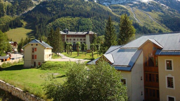 A mountain lodge with a central building surrounded by smaller structures, set against a backdrop of snow-capped mountains and dense forest. - 10m from resort center, 3rd floor, balcony, parking, tv, 20m², Pralognan-la-Vanoise (Pralognan-la-Vanoise)