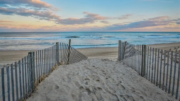 Een strand met een houten hek dat naar het water leidt, zandstrand en een heldere lucht.