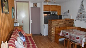 A compact living space with a kitchenette, a dining area, and a sofa with a plaid blanket.