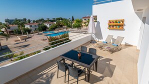 A balcony with a table and chairs, a pool, and a view of the surrounding area. - Narcissos 'Nissi Beach' apartment C12 (Ayia Napa)