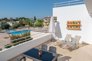 A balcony with a pool, lounge chairs, a table, and a potted plant.