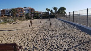 A sandy beach with a fence, palm trees, and a row of buildings in the background. - Extraordinary duplex in Naturist area (Vera)