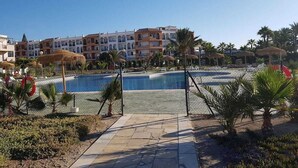 A resort pool area with a clear view of the pool, palm trees, and a building with multiple balconies in the background. - Extraordinary duplex in Naturist area (Vera)