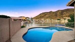 Ein Pool mit geschwungener Kante, umgeben von einem weißen Zaun, mit Blick auf eine hügelige Landschaft im Hintergrund.