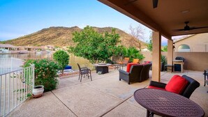 Eine überdachte Terrasse mit Gartenmöbeln, Blick auf einen Fluss und eine Hügelkulisse im Hintergrund.