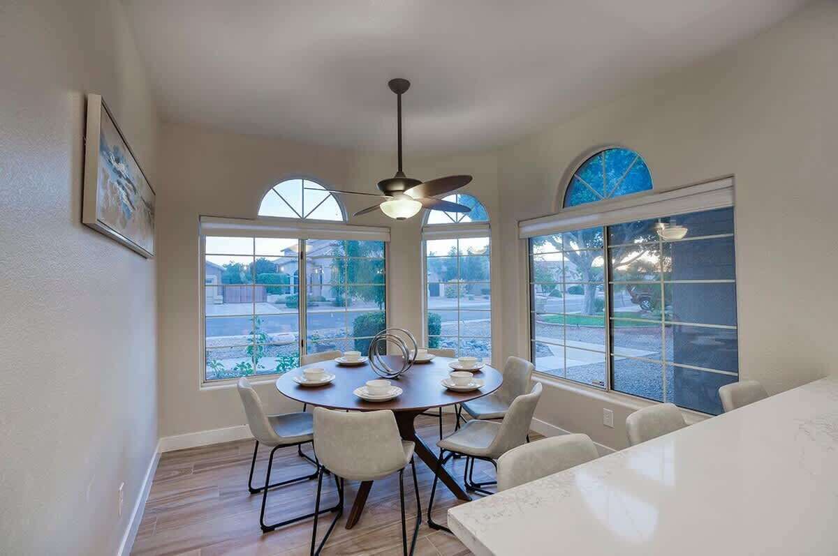 A dining area with a round table, white chairs, and a ceiling fan.