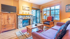 A cozy living room with a fireplace, a television, and a large window offering a view of the outside. - Stunning mountain view, free wifi, underground parking (copper mountain)