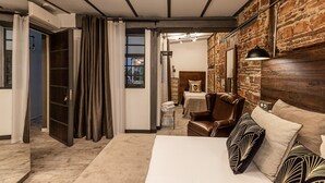 A modern bedroom with a brick wall, a large bed, a leather armchair, and a small table.
