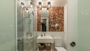 A modern bathroom with a glass-enclosed shower, a white sink, and a brick accent wall.