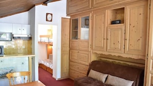 Ein gemütliches Zimmer mit einem Holzkasten, einem Bett, einem Esstisch und einer Mikrowelle.