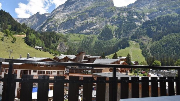 Blick auf Berge mit einem Chalet im Vordergrund, einer Seilbahn und einem Berggipfel im Hintergrund.