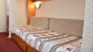 Ein kleiner, gemütlicher Raum mit einem Einzelbett, einem hölzernen Kopfteil und einer Wandleuchte.