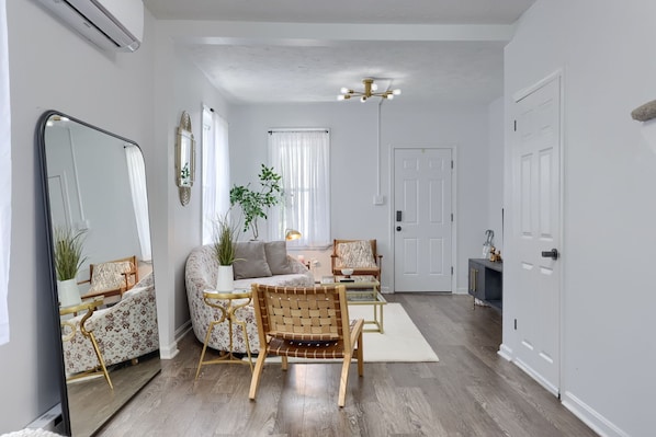A living room with a sofa, two chairs, a coffee table, a mirror, a plant, and a door.