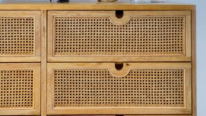Un aparador de madera con un televisor encima, un colgador de macramé y objetos decorativos.