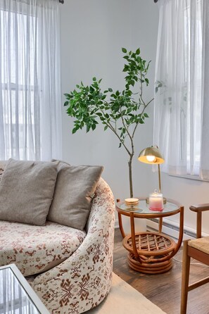 A living room with a sofa, a small table with a lamp, a potted plant, and a chair.