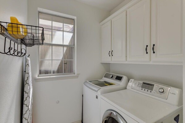 A laundry room with a washing machine, dryer, and a window with a curtain.