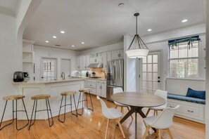 A modern kitchen with white cabinetry, a stainless steel refrigerator, and a round dining table with white chairs.