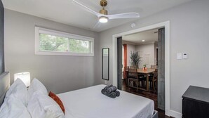 Une chambre à coucher avec un lit, un ventilateur de plafond, une fenêtre et une vue sur la salle à manger.