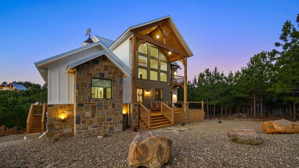 A two-story stone house with a balcony, a stone staircase, and a gravel driveway.