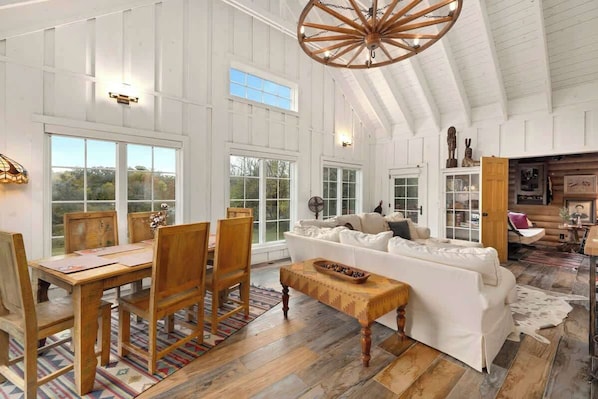 A spacious room with a high ceiling, wooden dining table, white sofa, and a large wooden ceiling fan.