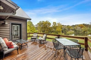 A wooden deck with outdoor furniture, a glass door, and a view of a lake and trees.