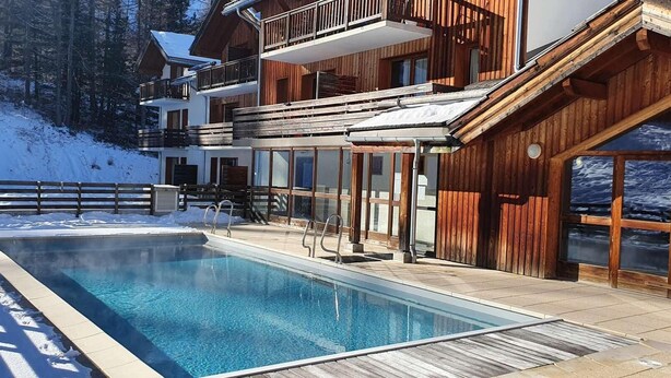 A modern building with a pool, wooden exterior, and balconies overlooking a snowy landscape. - Ski-in/ski-out & foot of the slopes, swimming pool, sauna, hammam, terrace, tv, ski locker, 43m² (Les Orres)