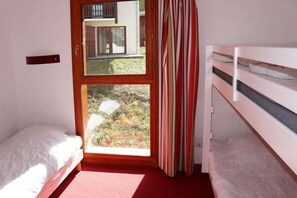 A room with two beds, a window with a view of a building and a garden, and a striped curtain. - Ski-in/ski-out & foot of the slopes, swimming pool, sauna, hammam, terrace, tv, ski locker, 43m² (Les Orres)