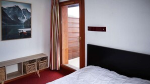 A bedroom with a bed, a wooden headboard, a bench with baskets, a painting of a mountain lake, and a sliding door to a balcony. - Ski-in/ski-out & foot of the slopes, swimming pool, sauna, hammam, terrace, tv, ski locker, 43m² (Les Orres)