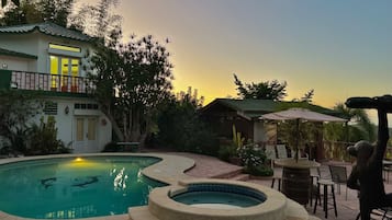 A swimming pool with a hot tub, surrounded by a patio area with outdoor seating and a building with a balcony.