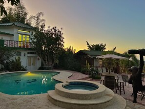 Una piscina con hidromasaje, rodeada de un patio con mobiliario exterior y un edificio con balcón.